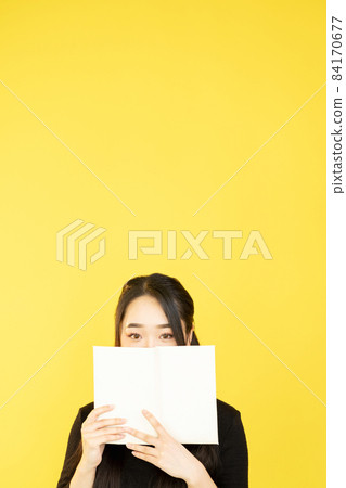 Girl student. School education. Reading hobby. Product advertising. Teen model hiding behind mockup blank book isolated on yellow empty space background. 84170677