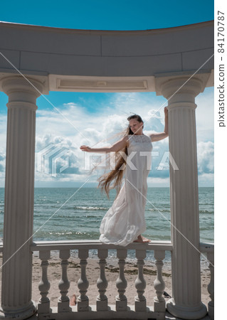 woman with long hair in white clothes is standing in the gazebo with snow-white columns woman with long hair in white clothes is standing in the gazebo with snow-white columns 84170787