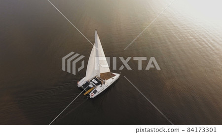 A small sailing yacht sails on the river at sunset 84173301