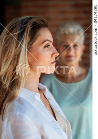 Senior mother looking at her adult daughter indoors at home. Selective focus on woman in foreground. 84174890