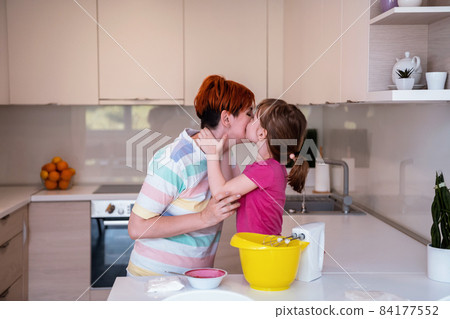 Funny little girl helper playing with dough on his hands learning to knead helps adult mom in the kitchen, happy cute baby daughter and parent mom have fun cooking cookies. 84177552