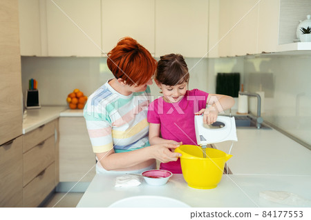Funny little girl helper playing with dough on his hands learning to knead helps adult mom in the kitchen, happy cute baby daughter and parent mom have fun cooking cookies. 84177553
