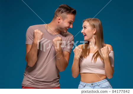 Overjoyed woman and man raise fists with triumph, have successful deal, exclaim joyfully, on blue background. Overjoyed woman and man raise fists with triumph, have successful deal, exclaim joyfully, on blue background. 84177842