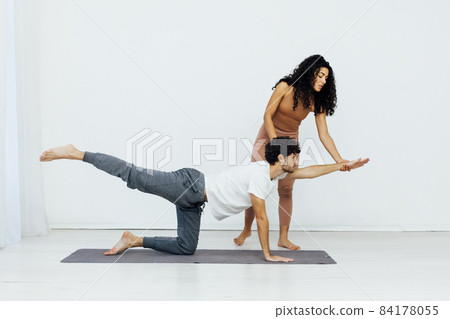 woman teaches man doing gymnastics yoga asana in a white room 84178055