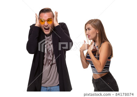 Angry blonde young European woman gestures with hands, shouts at husband who is guilty, stands together against white background, have dispute and quarrel Angry blonde young European woman gestures with hands, shouts at husband who is guilty, stands together against white background, have dispute and quarrel 84178074