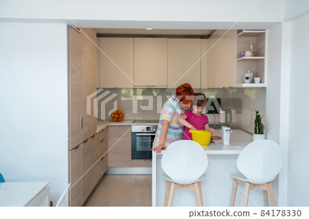 Funny little girl helper playing with dough on his hands learning to knead helps adult mom in the kitchen, happy cute baby daughter and parent mom have fun cooking cookies. 84178330