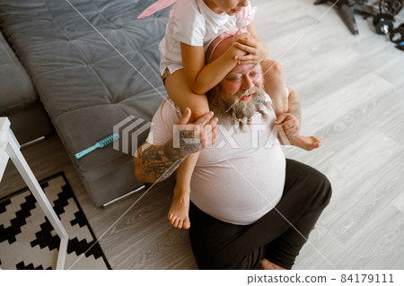 Daughter sits on shoulders of positive plump father in living room 84179111