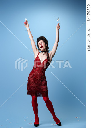 Portrait of young adorable gorgeous woman in dark red, wine color evening dress celebrating holiday isolated on blue background. 84179830