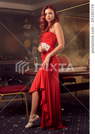 Charnimg sexy woman is posing against a poker table in luxury casino. Charnimg sexy woman is posing against a poker table in luxury casino. 84180159