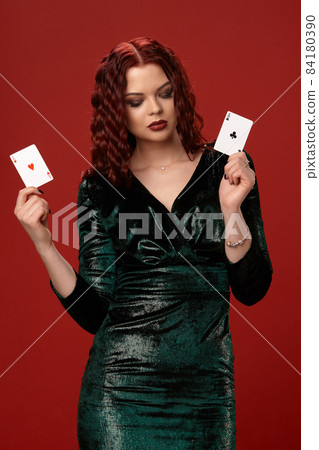 Young sexy woman with a red curly hair holding aces, on a red background. Poker 84180390