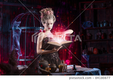 Charming woman witch flowers in hair vintage black dress with book of spell in the old castle. Halloween. Celebration. Charming woman witch flowers in hair vintage black dress with book of spell in the old castle. Halloween. Celebration. 84180877