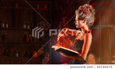 Charming woman witch flowers in hair vintage black dress with book of spell in the old castle. Halloween. Celebration. Charming woman witch flowers in hair vintage black dress with book of spell in the old castle. Halloween. Celebration. 84180878
