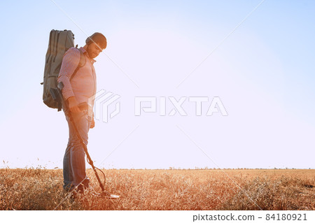 Man with metal detector equipment searching for metal goods in the field 84180921