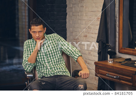 Handsome young man looking at the camera and sitting in a chair on at the barbershop 84181705
