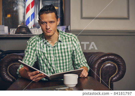Handsome young man in a barbershop is waiting for the master in the waiting room while drinking coffee 84181797