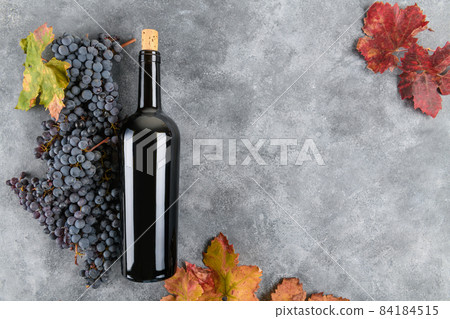 Red wine bottle with bunch of grape, fall grape's leaves on gray background, top view 84184515