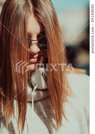 a modern girl with sunglasses walking down the street listens to music in headphones. 84189690