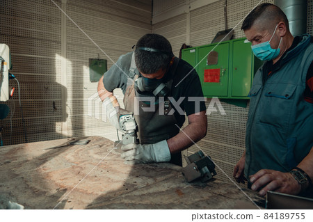 Industrial work during a pandemic. Two men work in a heavy metal factory, wearing a mask on their face due to a coronavirus pandemic 84189755