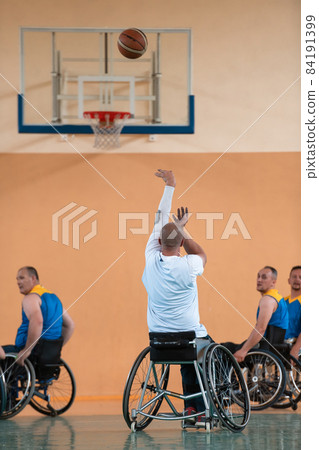 Disabled War veterans mixed race and age basketball teams in wheelchairs playing a training match in a sports gym hall. Handicapped people rehabilitation and inclusion concept Disabled War veterans mixed race and age basketball teams in wheelchairs playing a training match in a sports gym hall. Handicapped people rehabilitation and inclusion concept 84191399