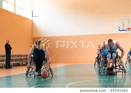 Disabled War veterans mixed race and age basketball teams in wheelchairs playing a training match in a sports gym hall. Handicapped people rehabilitation and inclusion concept 84191463