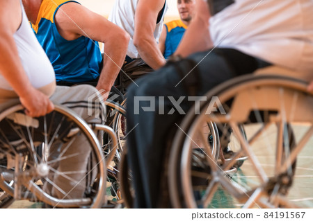 Close up photo of wheelchairs and handicapped war veterans playing basketball on the court 84191567