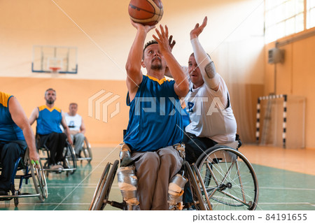 Disabled War veterans mixed race and age basketball teams in wheelchairs playing a training match in a sports gym hall. Handicapped people rehabilitation and inclusion concept Disabled War veterans mixed race and age basketball teams in wheelchairs playing a training match in a sports gym hall. Handicapped people rehabilitation and inclusion concept 84191655