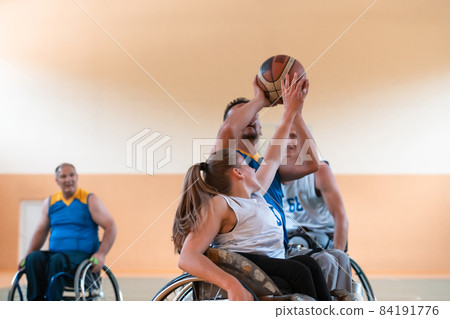 Disabled War veterans mixed race and age basketball teams in wheelchairs playing a training match in a sports gym hall. Handicapped people rehabilitation and inclusion concept Disabled War veterans mixed race and age basketball teams in wheelchairs playing a training match in a sports gym hall. Handicapped people rehabilitation and inclusion concept 84191776