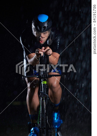 triathlon athlete riding bike fast on rainy night 84191786