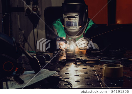 A woman employed in a modern factory for the production and processing of metals in a work uniform welding metal materials A woman employed in a modern factory for the production and processing of metals in a work uniform welding metal materials 84191806