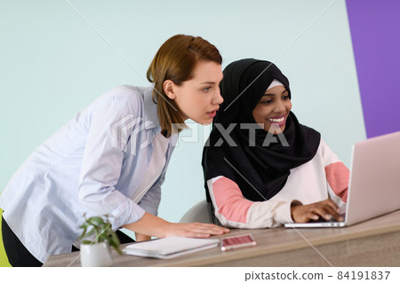 afro muslim woman wearing a hijab sits smiling in her home office and using laptop for online meeting afro muslim woman wearing a hijab sits smiling in her home office and using laptop for online meeting 84191837