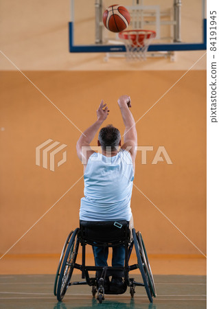a war invalid in a wheelchair trains with a ball at a basketball club in training with professional sports equipment for the disabled. the concept of sport for people with disabilities 84191945
