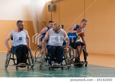 Disabled War veterans mixed race opposing basketball teams in wheelchairs photographed in action while playing an important match in a modern hall.  84192000