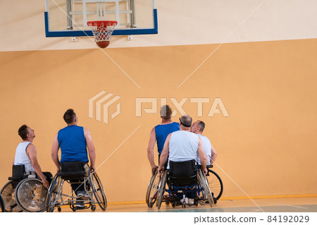 Disabled War veterans mixed race opposing basketball teams in wheelchairs photographed in action while playing an important match in a modern hall. Disabled War veterans mixed race opposing basketball teams in wheelchairs photographed in action while playing an important match in a modern hall. 84192029