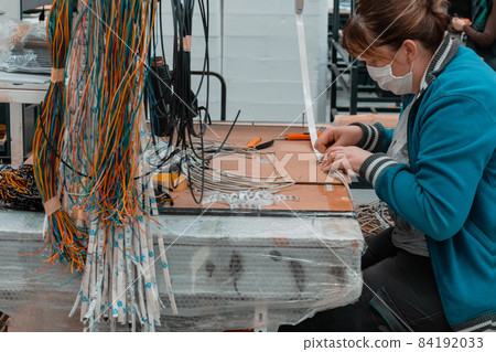 Industrial worker wearing a face mask due to a coronavirus pandemic solders cables from factory production equipment 84192033
