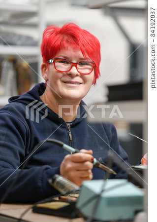 Industrial worker woman soldering cables of manufacturing equipment in a factory Industrial worker woman soldering cables of manufacturing equipment in a factory 84192037