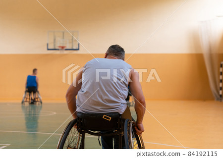Close up photo of wheelchairs and handicapped war veterans playing basketball on the court 84192115