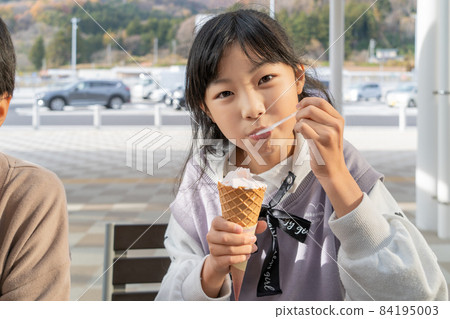 Elementary school girl eating soft serve ice cream in the service area Elementary school girl eating soft serve ice cream in the service area 84195003