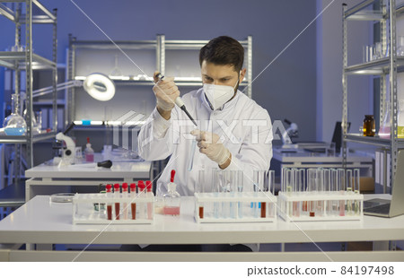 Serious cautious man scientist with pipette adds liquid to test tube in medical laboratory. Portrait of man watching interaction of chemical components. Concept of scientific medical research. Serious cautious man scientist with pipette adds liquid to test tube in medical laboratory. Portrait of man watching interaction of chemical components. Concept of scientific medical research. 84197498