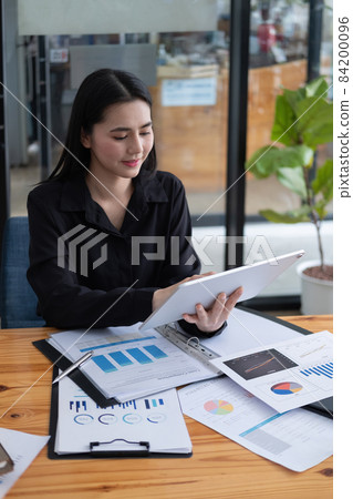 Attractive businesswoman using a digital tablet while working with paperwork financial data chart on wooden desk. Attractive businesswoman using a digital tablet while working with paperwork financial data chart on wooden desk. 84200096