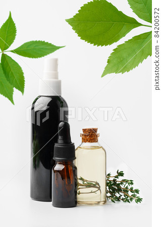 Essential oil in a small bottle with green leaf on white background 84200572