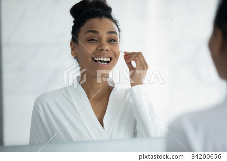 Happy young african american woman cleaning ears with cotton swab. Happy young african american woman cleaning ears with cotton swab. 84200656
