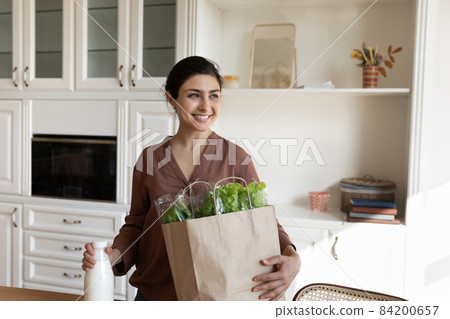 Woman standing in kitchen with shopping bag full with groceries 84200657