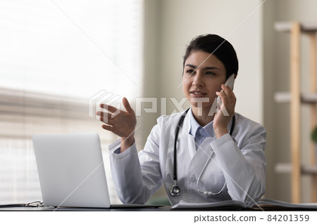 Smiling Indian woman doctor talking on phone, consulting patient 84201359