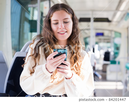 Portrait of a positive girl on public transport and texting on a mobile phone Portrait of a positive girl on public transport and texting on a mobile phone 84201447