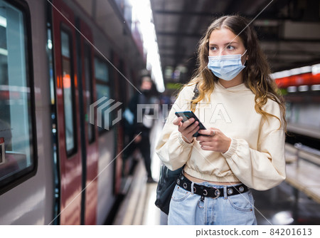 Young woman in mask using mobile phone while waiting metro Young woman in mask using mobile phone while waiting metro 84201613