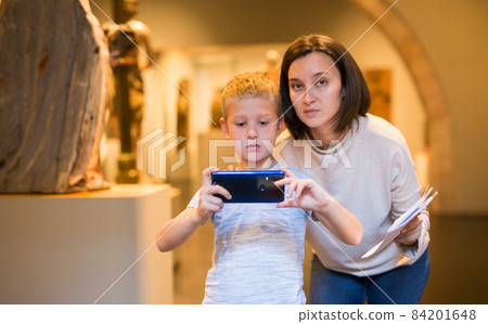 Boy using phone while in museum Boy using phone while in museum 84201648