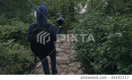Traveler photographing scenic view in forest. One caucasian woman shooting nice magic look. Girl take photo video on dslr mirrorless camera. 84202517
