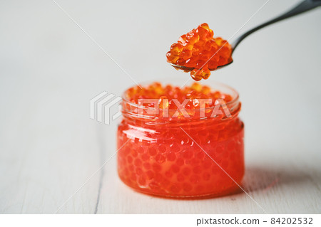 Open jar with red caviar and a spoon above it Open jar with red caviar and a spoon above it 84202532