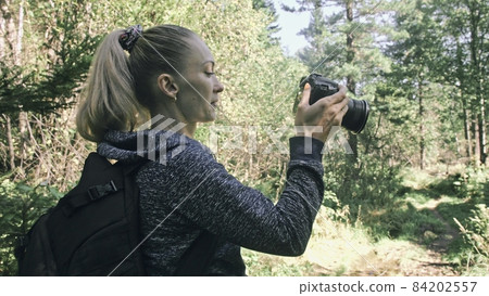 Traveler photographing scenic view in forest. One caucasian woman shooting nice magic look. Girl take photo video on dslr mirrorless camera. 84202557