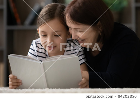Smiling mature grandmother with little girl reading book together 84202856
